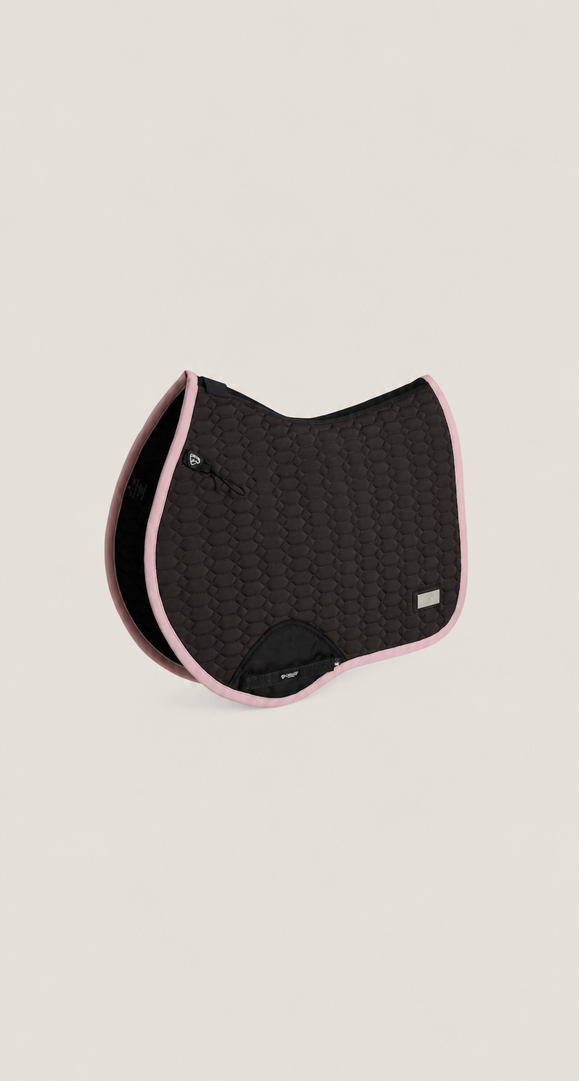 A black quilted equestrian saddle pad with light pink trim, shown on a solid light beige background.