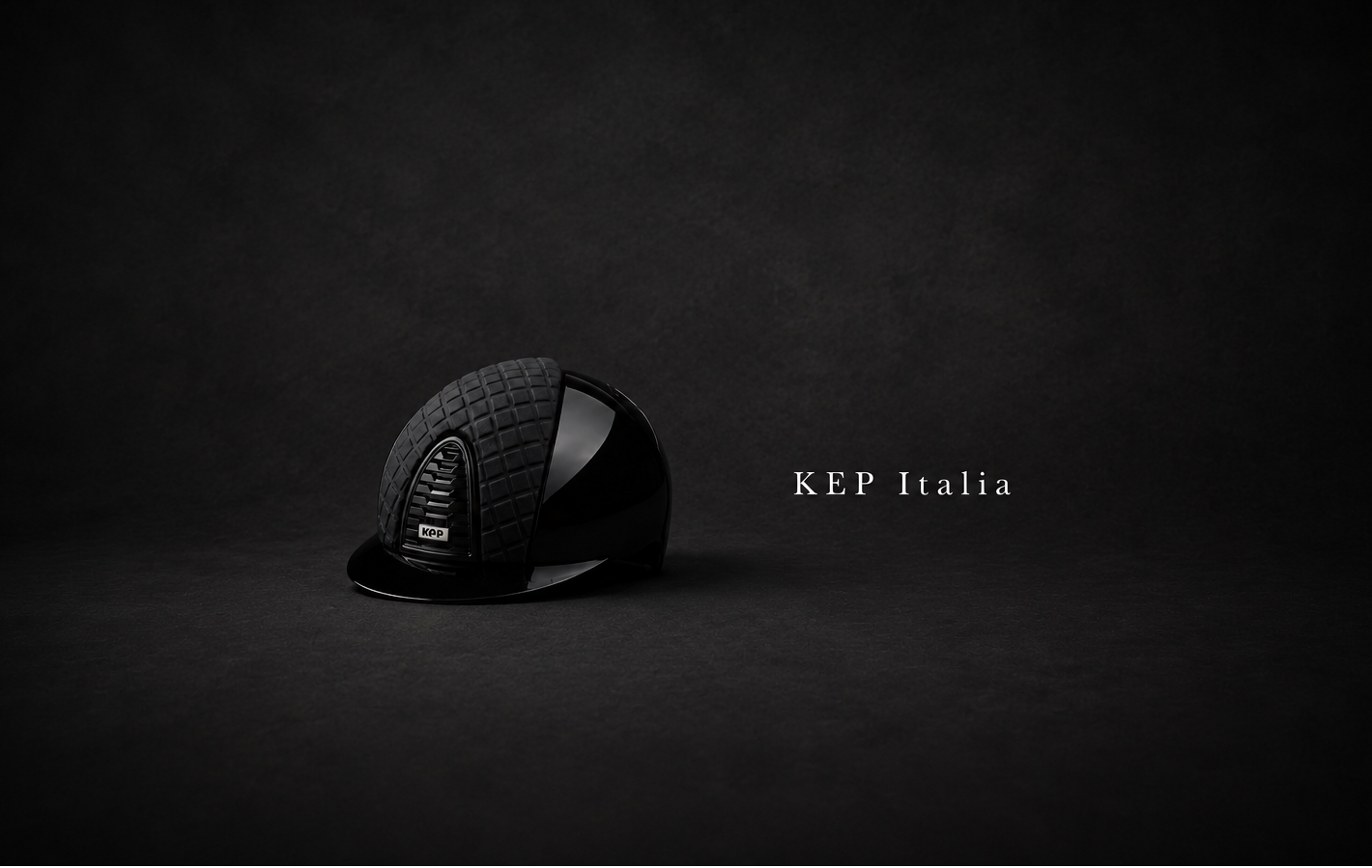 A black equestrian riding helmet with a textured crown and glossy visor, displayed on a dark studio background with the text 'KEP Italia' to the right.